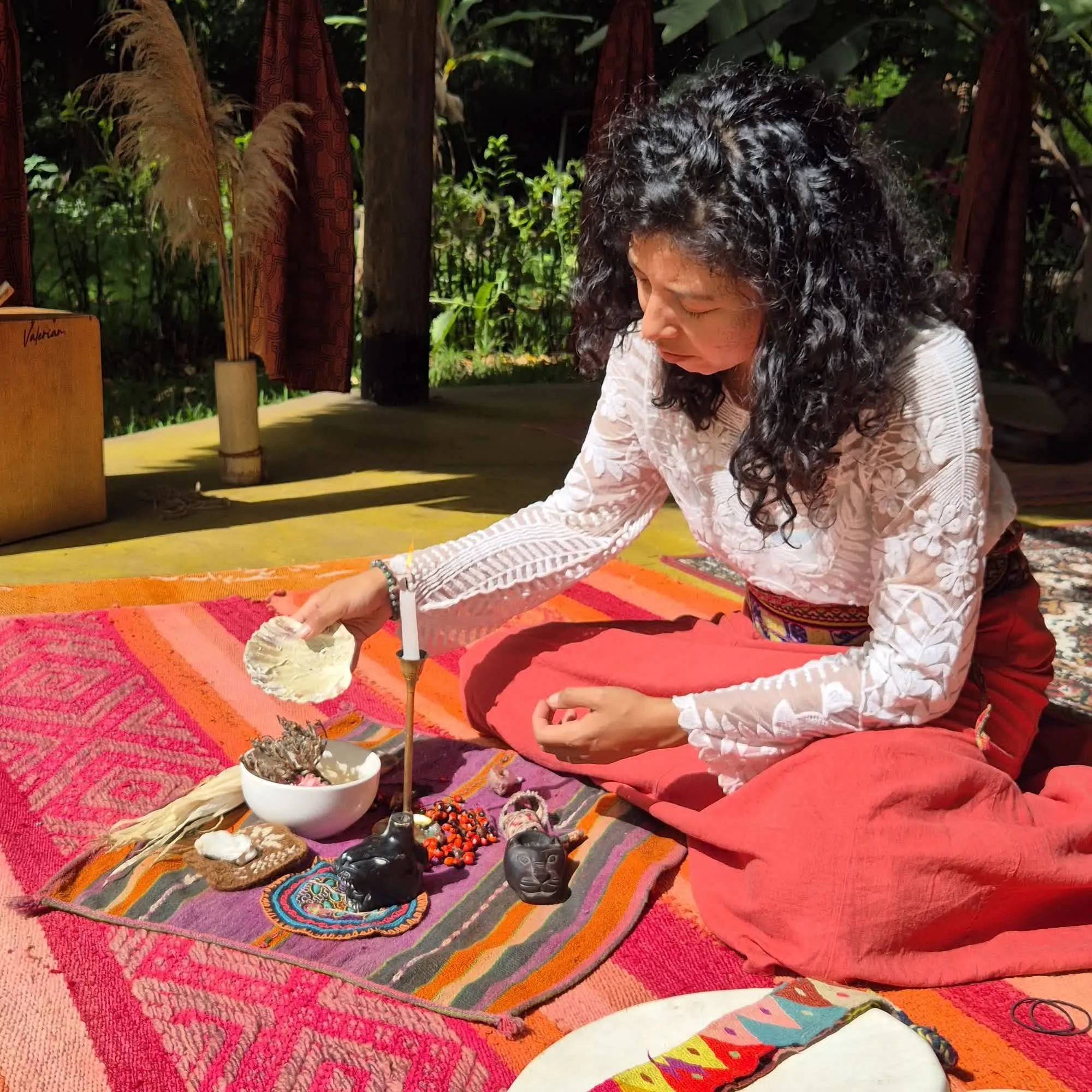 Mar arranging a ceremonial offering — flowers, sacred objects, and prayer items on woven textile